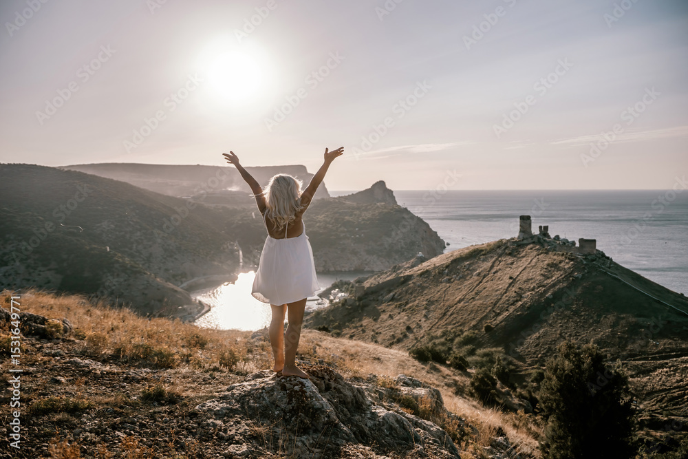 A woman is standing on a hill overlooking a body of water. She is wearing a white dress and she is happy. A woman is standing on a hill overlooking a body of water. She is wearing a white dress and she is happy.