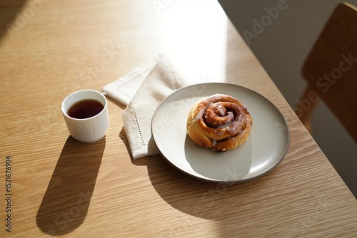 Fresh cinnamon roll on a plate with cup of black coffee in morning sunlight photo