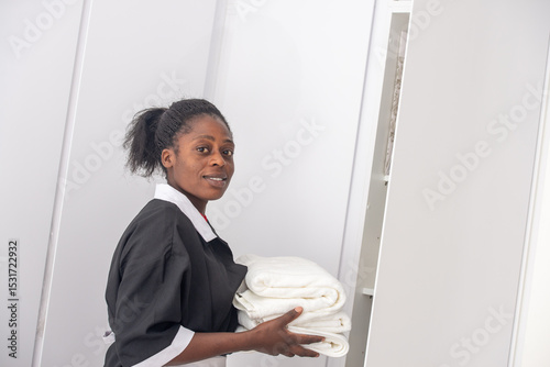 Portrait of an African woman housekeeper in uniform holding neatly folded towels.