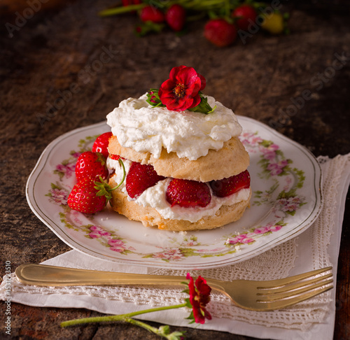 Homemade strawberry shortcake topped with whipped cream and a small red flower from a strawberry plant; copy space