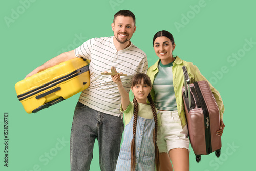Family of tourists with wooden airplane and suitcases on green background