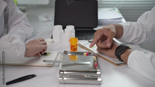 Two doctors are sitting at a desk with a bottle of pills in front of them