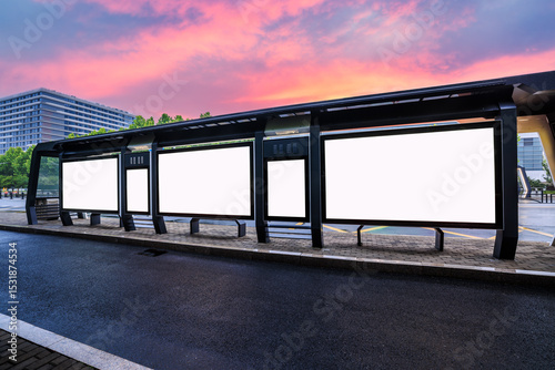 Fototapeta Naklejka Na Ścianę i Meble -  Modern bus stop shelter with multiple blank white billboards for advertising mockup on urban street at sunset