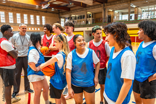 Fototapeta Naklejka Na Ścianę i Meble -  Diverse high school basketball team listening to coach's instructions in gym