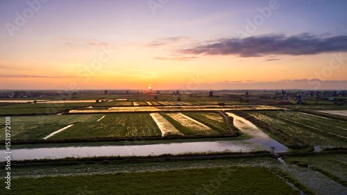 A serene sunset over lush rice fields with reflective water channels and distant windmills