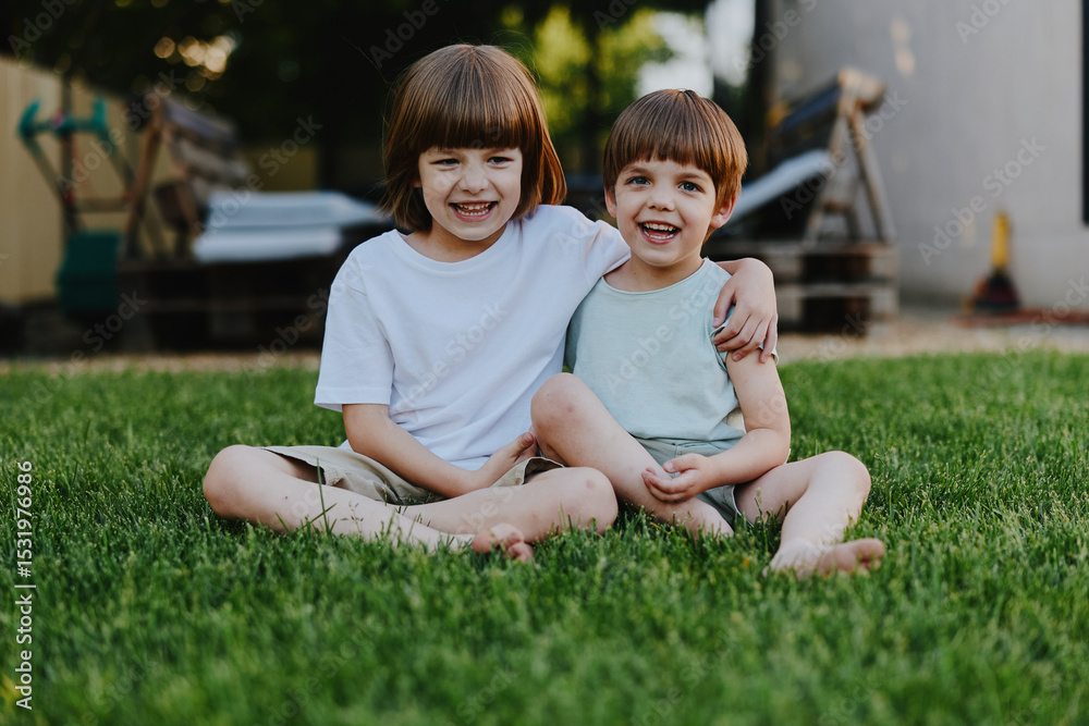 Fototapeta premium Happy children sitting on green grass, enjoying a sunny day while smiling and playing together in a cheerful outdoor setting, capturing moments of childhood joy.