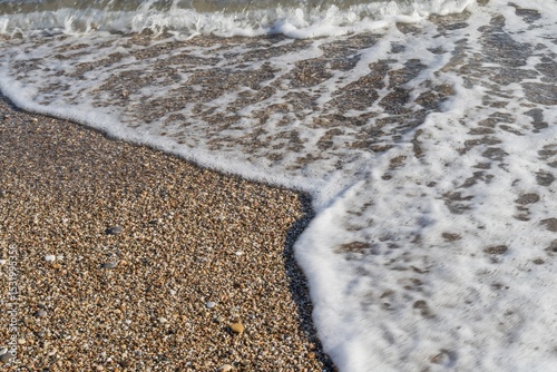 Fototapeta Naklejka Na Ścianę i Meble -  Close-up of gentle sea wave rolling on sandy shore. Sparkling sea water and foam on shore at sunset