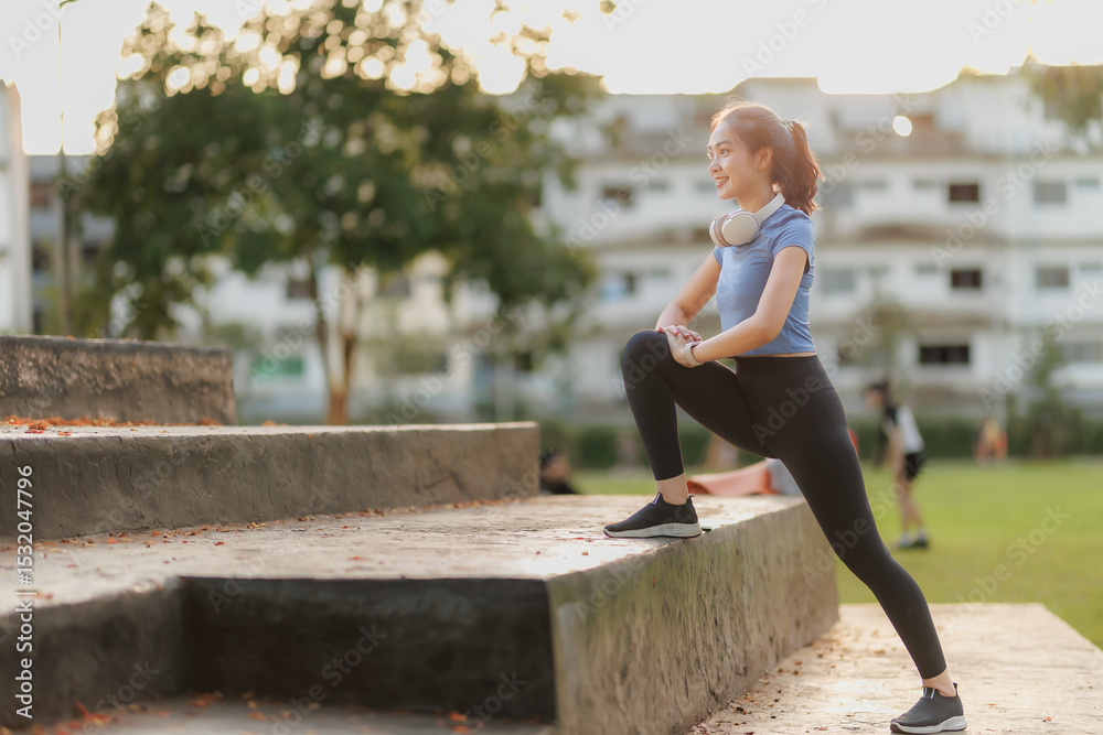 Fototapeta premium A young woman takes a break after exercising, relaxing with a cheerful smile. She wears headphones, listens to music, and chats with her friend on the phone, enjoying the peaceful moment.
