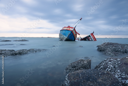 Old wrecked fishing boat in sea at dusk on coast of Ang Sila Village, Saensuk Sub-district, Chonburi Province of thailand. Suite for feelings of loss, disappointment, loneliness, emptiness and storm.