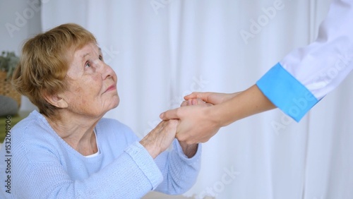 Young nurse is providing comfort and support to an elderly woman by gently holding her hands, offering reassurance and care in a healthcare setting
