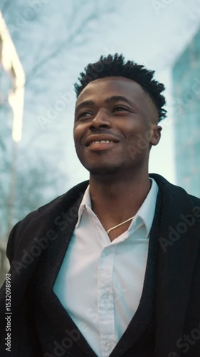 Vertical portrait of self-confident african male person walking in city center in daytime. Successful businessman strolling outdoors and smiling, enjoy life and feel good, positive emotions, black guy