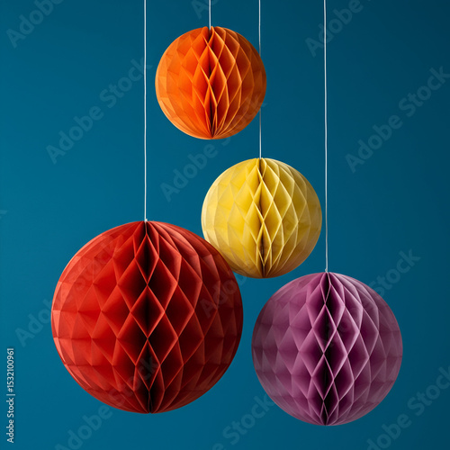 Multicolored paper honeycomb spheres hanging on strings against a teal background.