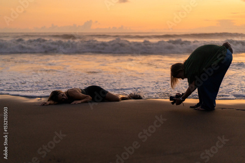 Photographer capturing woman lying on beach at sunset