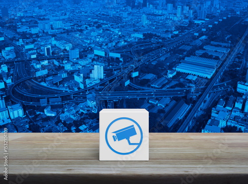 Cctv camera flat icon on white block cube on wooden table over modern city tower, street, expressway and skyscraper, Technology security and safety online concept