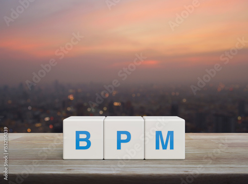 BPM acronym on white block cubes on wooden table over blur of cityscape on warm light sundown, Business process management concept