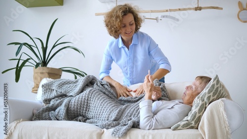 Obraz na plátne Smiling nurse covering elderly woman with a cozy blanket while checking her temp
