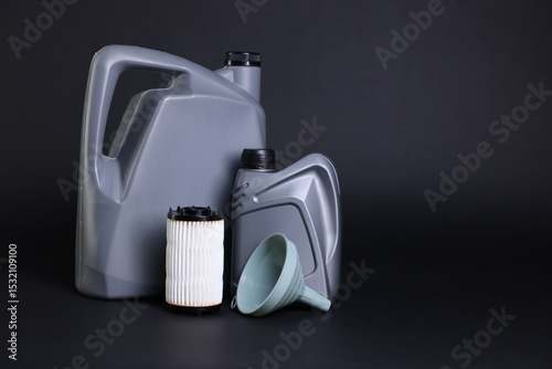 Fototapeta Naklejka Na Ścianę i Meble -  Motor oil in plastic canisters, filter and funnel on black background, space for text