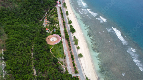 Aerial birds eye view of green trees, park, white sandy beach, and turquoise ocean in capital city Dili, Timor-Leste, Southeast Asia