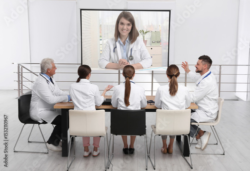 Team of doctors using video projector during conference indoors. Speaker on projection screen