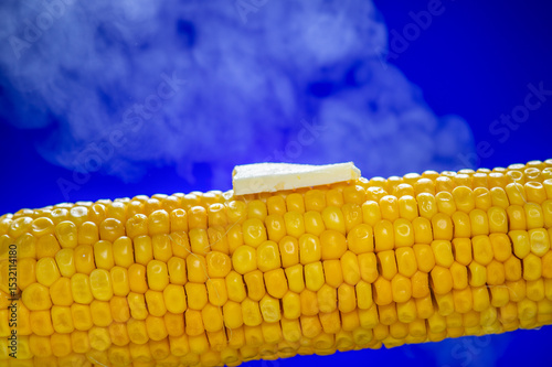 Delicious yellow corn on the cob with a melting piece of butter on top, placed against a vibrant blue background.