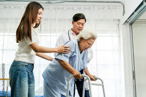 Obraz na plátne An elderly woman receives support from a doctor and a young caregiver as she uses a walker to stand