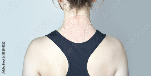 Caucasian female with therapeutic kinesiology tape on upper back for muscle support.