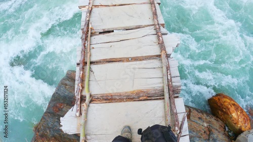 4K POV of hiker woman crossing wooden bridge over a Beas river in Manali, Himachal Pradesh, India. Top view of woman legs in hiking shoes. Travel and Adventure in nature. 