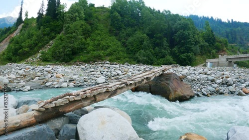 4K shot of Beautiful wooden pedestrian bridge over a fast mountain river at Manali, Himachal Pradesh, India. Beas river in Solang Valley during summer season. Nature and travel background.
