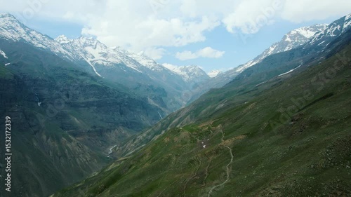 4K Aerial shot of snow capped mountains and hiking trail in Ghepan Trek, Lahaul, India. Clouds in sky and Himalaya mountains during summer season. Mountain road and beautiful landscape