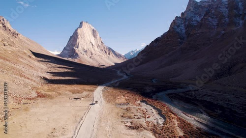 4K Aerial shot of mighty Gonbo Rangjon mountain peak and vehicle passing on road at Zanskar, Ladakh, India. Remote Himalayan mountain range. Zanskar during Summer day. Travel and holiday concept.