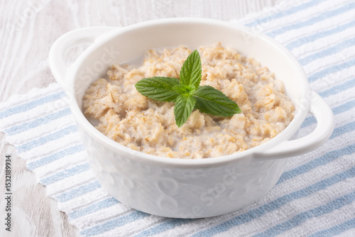 Oatmeal porridge in white bowl, close up view.