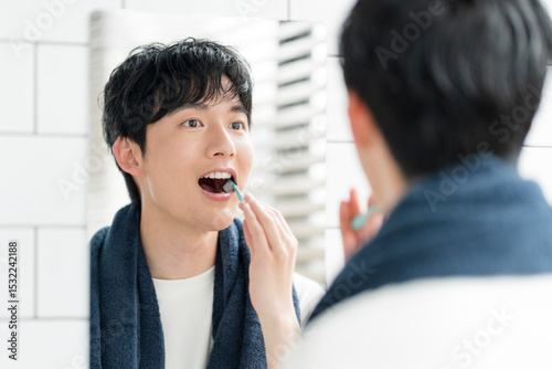 洗面所で鏡を見ながら歯を磨いている若い日本人男性