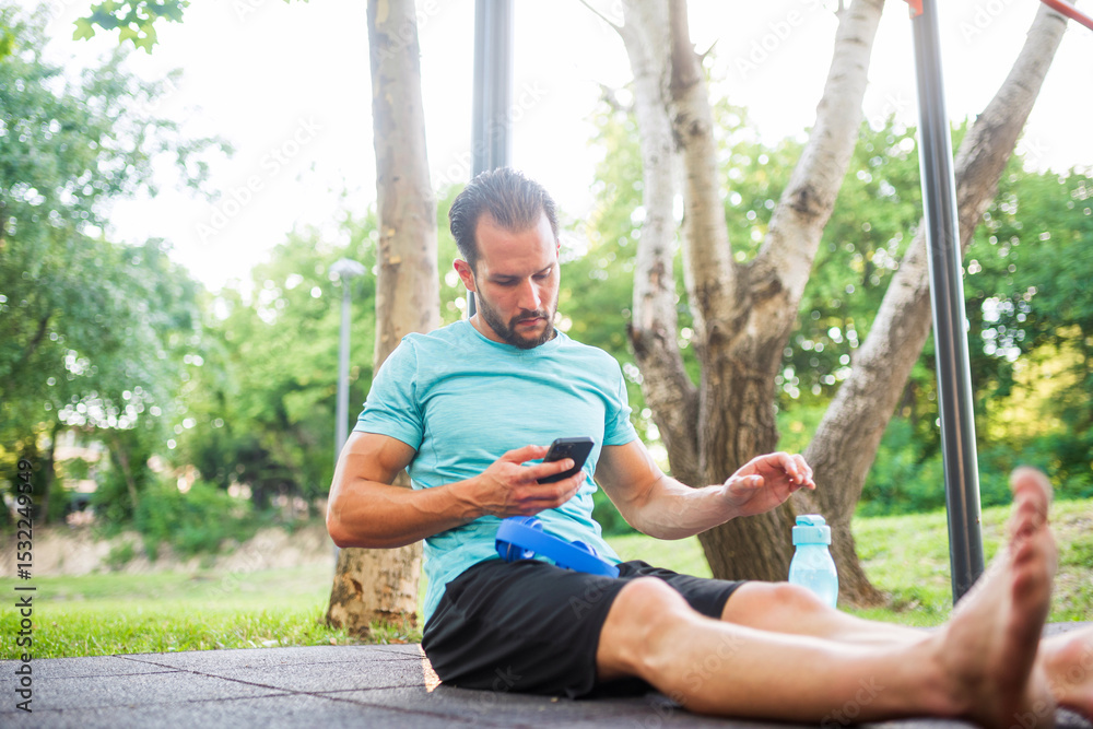 Naklejka premium Athletic man using smartphone at outdoor gym