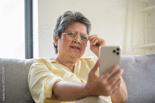Senior people lifestyle health problem concept : Portrait photo of senior Asian woman has an eye long sighted problem trying to read message from smartphone monitor.