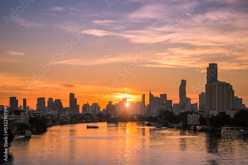 Sunrise over Chao Phraya River in Bangkok with golden skyline tall buildings reflecting in water.