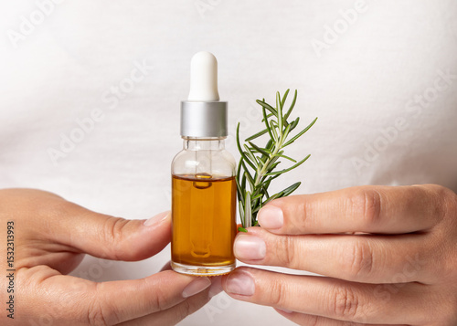 Closeup of female hands holding small dropper oil bottle and fresh rosemary sprigs