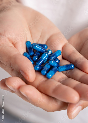 Cupped female hands with a pile of blue medical herbal capsules closeup over white shirt