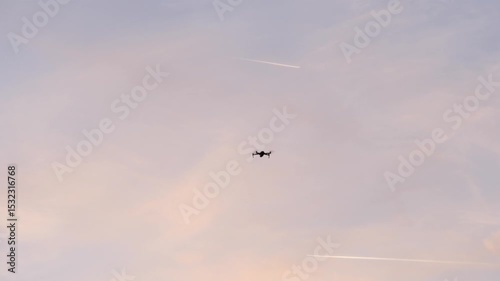 High above, a lone drone hovers, its dark outline contrasting against an airline