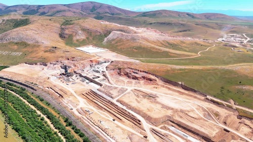 Construction of a cement plant in the mountains, aerial view. Earthworks, heavy machinery, and rail access visible along the site.