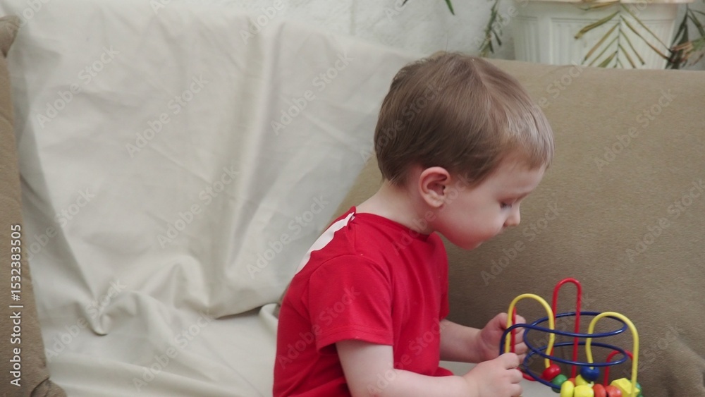 Naklejka premium Happy baby play educational toys. Portrait of a smiling child playing while sitting on the sofa. Kid about one two years old. baby at home playing with toys
