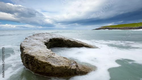 Coastal Serenity: A weathered stone structure, gracefully embraces the tide, a timeless monument to the ocean's touch, as clouds drift in the expansive sky, capturing a moment of enduring calm.