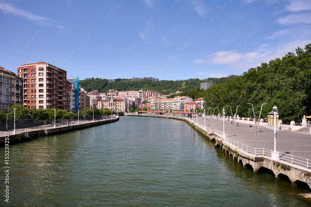 Obraz premium Scenic view of Nervion river, residential buildings, and promenade in Bilbao, spain, on a sunny summer day
