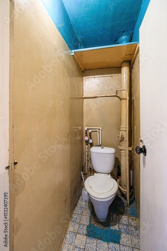 Photography interior shot of a small, outdated bathroom with a white toilet