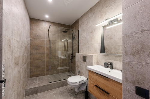 Modern bathroom with earth-tone tiles, glass shower, and wooden vanity. Minimalist design with black fixtures