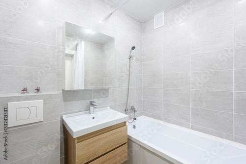well-lit, modern bathroom featuring gray tiles, a wooden sink cabinet, a white bathtub, and a mirror