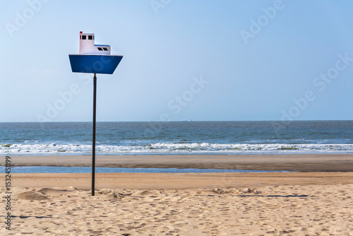 Wooden model of a blue and white boat on pole on a sandy beach, coastal village De Haan, West Flanders, Belgium