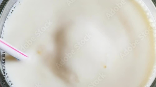 A straw bubbling in a milkshake, bubbles visible from top view – video