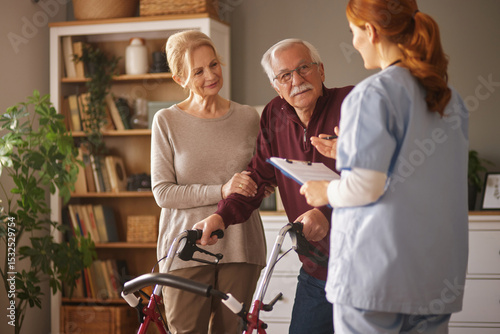 A home healthcare nurse in scrubs holds a clipboard and speaks with an elderly man, who is using a walker, and his wife in their living room, during a home care visit.