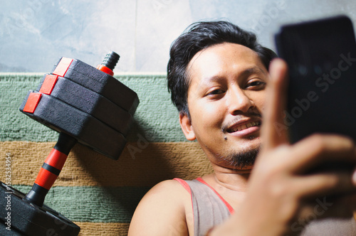 Man Relaxing After Exercise While Browsing Phone Beside Fitness Dumbbells