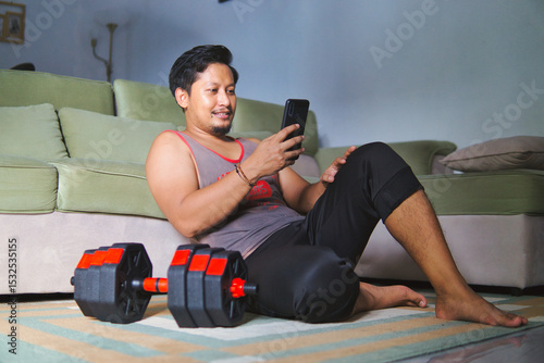 Man Relaxing After Workout Holding Smartphone Beside Dumbbell in Living Room